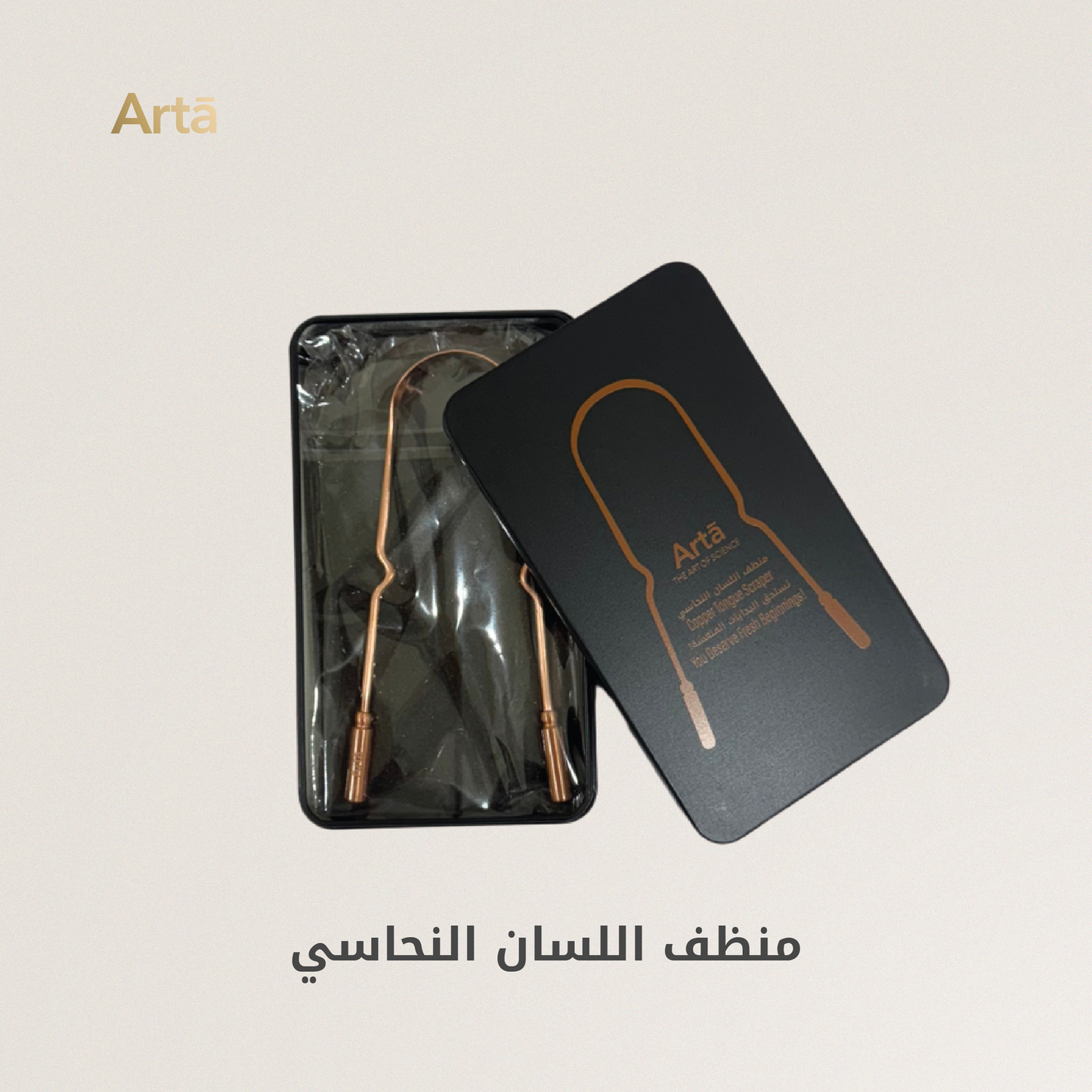 A copper tongue scraper by ArtŤ placed on an orange surface, with a grey case bearing the brand name 'ArtŤ' in the background.