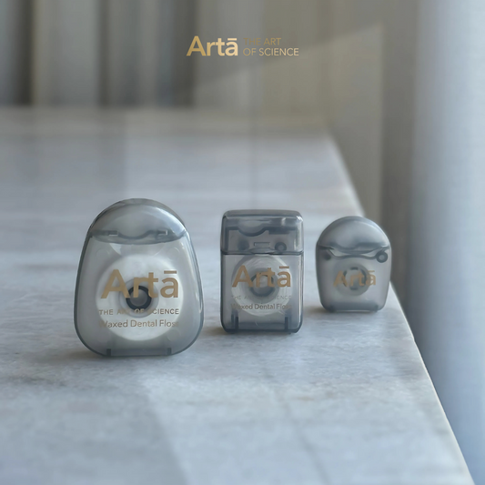 Three containers of PTFE waxed dental floss with the brand 'Artà' displayed on them, placed on a marble surface.