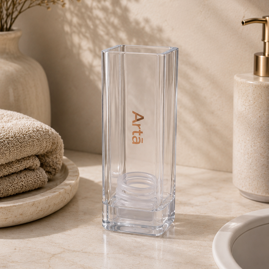 Clear glass vase with 'Arta' branding on a bathroom counter.