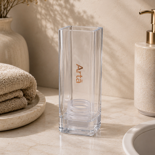 Clear glass vase with 'Arta' branding on a bathroom counter.